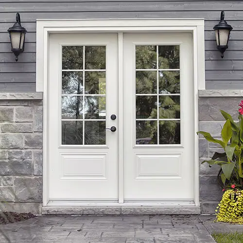 Porte de jardin double blanche style porte française avec grilles Vaillancourt Portes et Fenêtres vue d’une cour de maison.