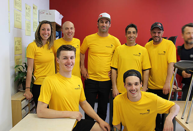 Sept collègues de chez Vaillancourt Portes et Fenêtres vêtus d’un chandail jaune de la compagnie dans un bureau au mur rouge