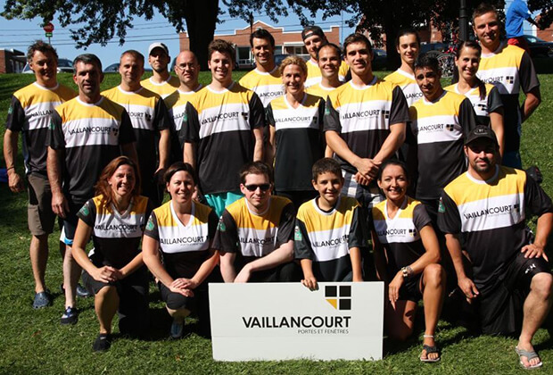 Group of employees wearing a black, white and yellow t-shirt from Vaillancourt Doors and Windows holding a sign with the logo