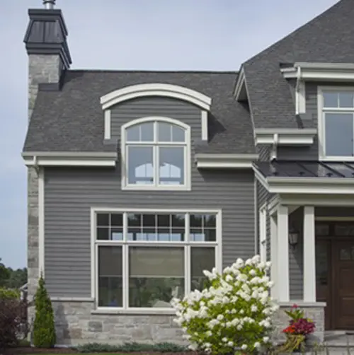 Vaillancourt Doors and Windows architectural white custom PVC and hybrid window on the cornice of a blue-grey house.